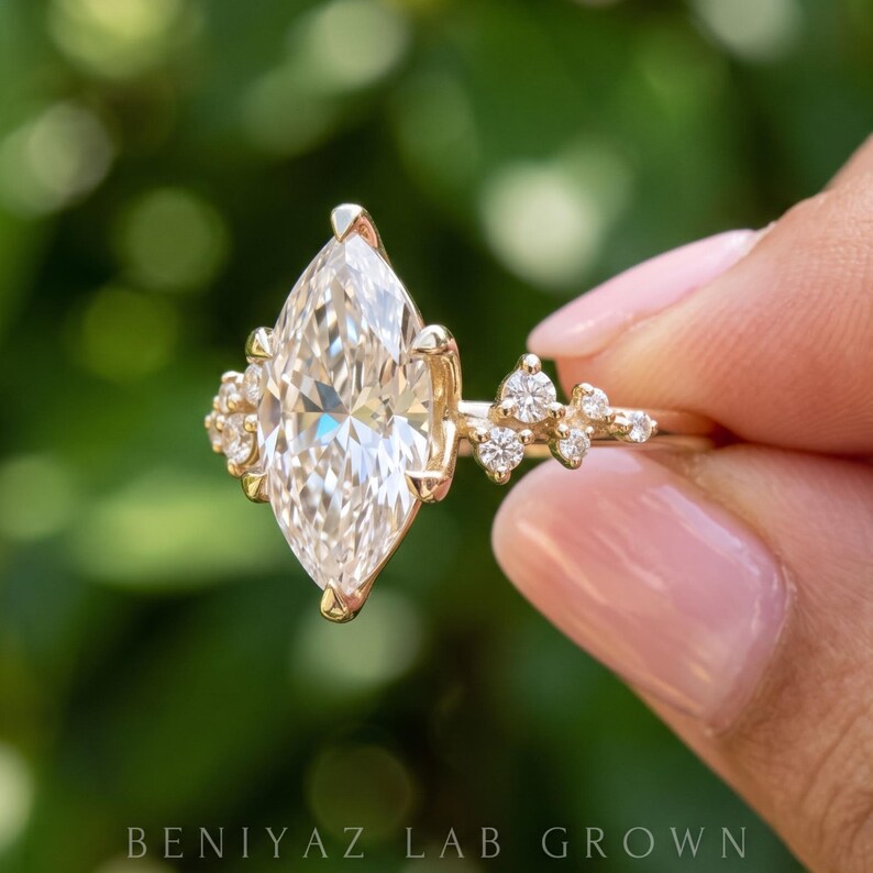 Marquise engagement ring held between fingertips, featuring a brilliant lab grown diamond center and ornate cluster setting.