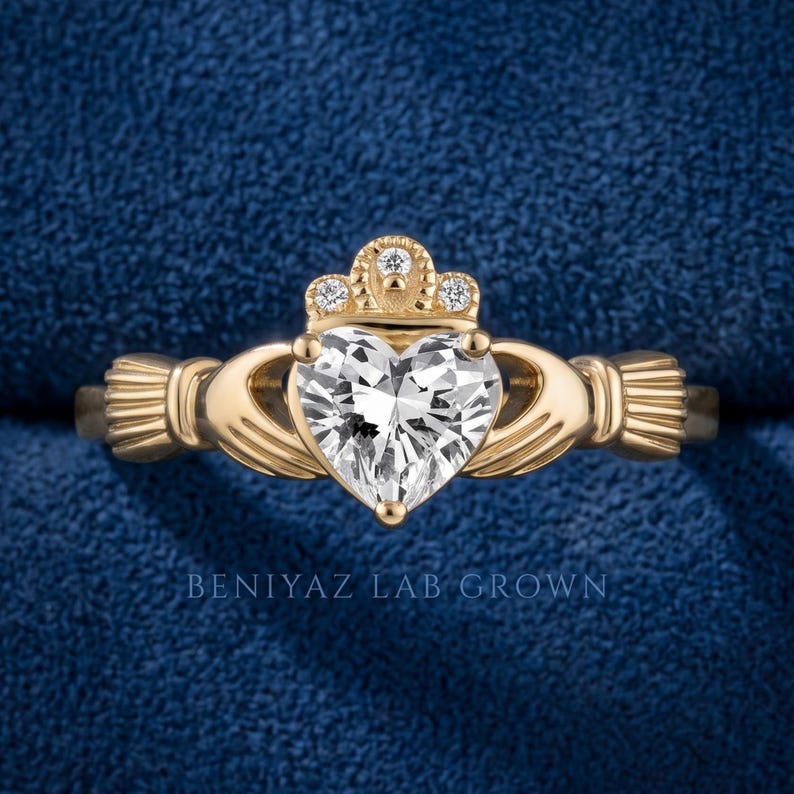 Close-up hand held Claddagh engagement ring with heart shaped lab grown diamond center, crown accents and polished yellow gold finish.