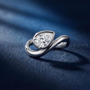 Pear cut lab grown diamond set in a smooth polished surround on a sculptural bypass ring, shown in an angled front view.