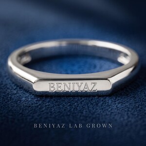 Custom engravable signet ring on a dark blue background showing the rectangular face and smooth polished band.