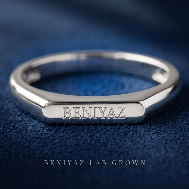 Custom engravable signet ring on a dark blue background showing the rectangular face and smooth polished band.