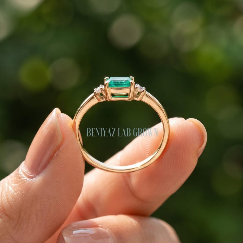 Rear view of lab grown emerald ring showing the slim solid gold shank, east west setting and three stone engagement ring design.