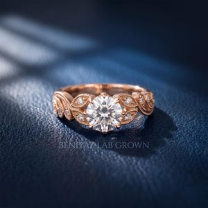 Close-up rose gold lab grown diamond engagement ring with a round brilliant center diamond, antique style leaf design, milgrain details and accent stones along the shoulders.