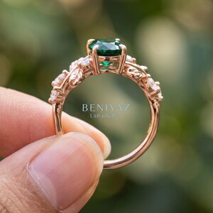 Angled side view of green stone ring with oval lab emerald center, leaf details and round accent stones.