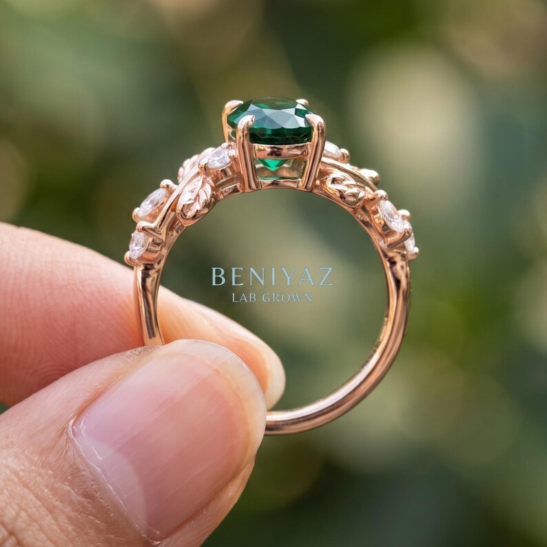 Angled side view of green stone ring with oval lab emerald center, leaf details and round accent stones.