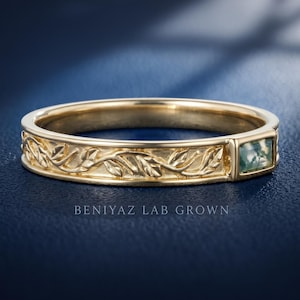 Puede incluir: Un anillo de oro con un patr&oacute;n de hojas en relieve a lo largo de la banda y una piedra de &aacute;gata musgosa rectangular engastada horizontalmente. El texto BENIYAZ LAB GROWN aparece debajo del anillo. La banda tiene un acabado met&aacute;lico pulido.