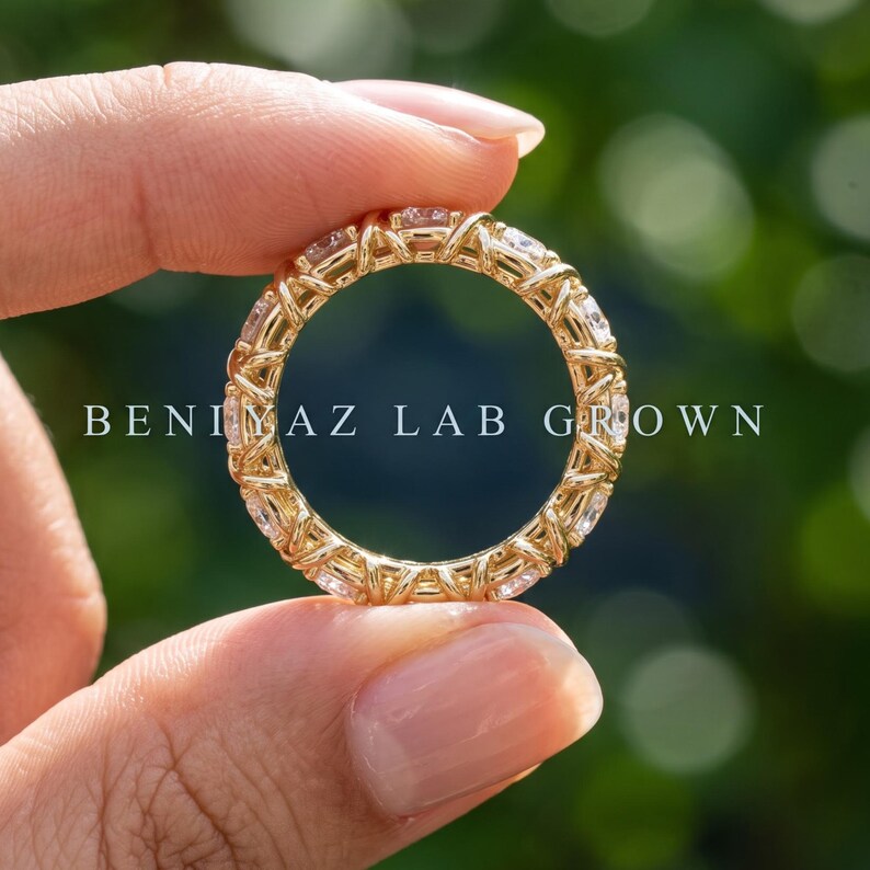 Hand-held rear view of the X crossover eternity ring showing the continuous full-circle design and polished gold-tone shank.