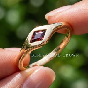 Detailed angled view of red stone ring with kite set burgundy gemstone, flush setting and minimalist gold tone band.