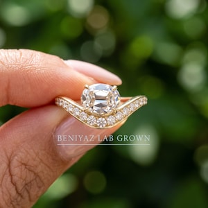Close up hand view of an antique style lab grown diamond ring in yellow gold, showing the side profile and elevated vintage inspired setting against a green background