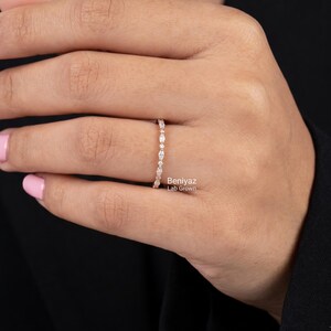 Elegant close-up of a woman's hand wearing a delicate marquise and round lab grown diamond wedding band against dark clothing. The thin ring features alternating brilliant diamond shapes along the top of a polished band. This minimalist half eternity ring is designed for everyday elegance, wedding jewelry, anniversary celebrations and stacking with an engagement ring.