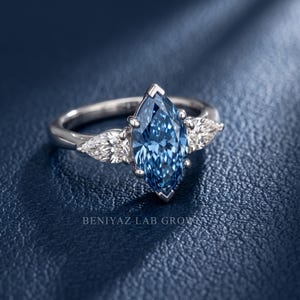 Angled studio view of a blue marquise diamond engagement ring with pear side stones and a slim polished three stone band.