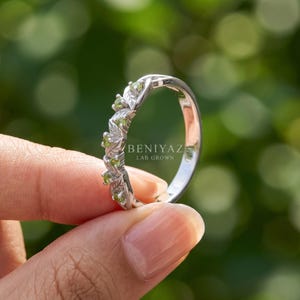 Woodland style peridot wedding band with green gemstones arranged through a flowing leaf and vine pattern.