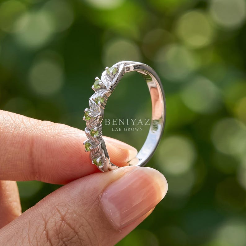 Woodland style peridot wedding band with green gemstones arranged through a flowing leaf and vine pattern.