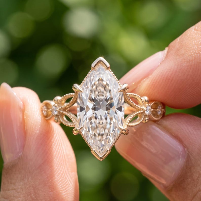 May include: A gold ring featuring a large marquise-cut center stone held by prongs. The band displays intricate filigree metalwork with small round accent stones embedded on each side, creating a detailed and ornate appearance.