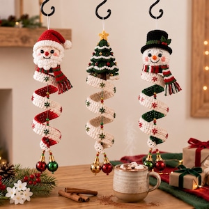 Può includere: Tre decorazioni natalizie all'uncinetto da appendere raffiguranti Babbo Natale, un albero di Natale verde e un pupazzo di neve. Ogni figura ha un lungo corpo a spirale in nastro bianco e rosso o verde, decorato con fiocchi di neve e sfere.
