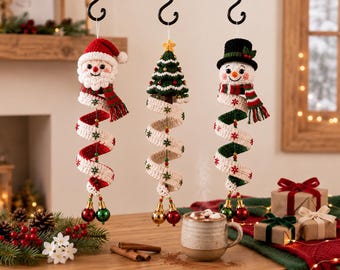 May include: Three hanging crochet Christmas ornaments featuring a Santa Claus, a green Christmas tree, and a snowman. Each figure has a long, spiraling white and red or green ribbon body decorated with small snowflakes and two dangling baubles.