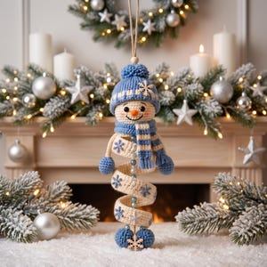 May include: A crocheted snowman ornament featuring a blue knit hat with a pom-pom and a matching blue and white striped scarf. The snowman has a spiral-shaped body in cream with blue snowflake accents, blue mittens, and a wooden snowflake charm.