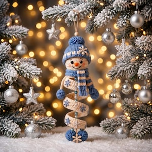 May include: A crocheted snowman ornament featuring a blue knit hat with a pom-pom, a matching striped scarf, and a spiral-shaped body in cream with blue snowflake accents. The snowman has a small orange nose and two blue pom-poms at the base.