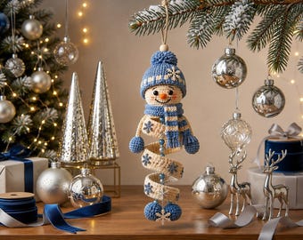 May include: A crocheted snowman ornament featuring a blue knit hat with a pom-pom, a matching blue and white striped scarf, and a spiral body in cream with blue snowflake accents. The snowman has a small orange nose and blue bead details.