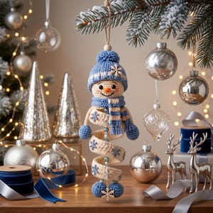 May include: A crocheted snowman ornament featuring a blue knit hat with a pom-pom, a matching blue and cream striped scarf, and a spiraling cream-colored body decorated with blue snowflake patterns, hanging from a natural twine loop.