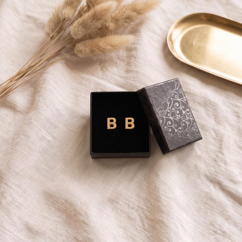 OraVero gift box with a pair of gold initial stud earrings set in black velvet, ready to give as a Christmas gift, shown on cream linen with dried pampas grass.