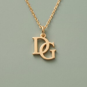 May include: A gold-toned necklace featuring a pendant shaped like the interlocking capital letters D and G. The pendant is suspended from a delicate gold-toned chain with small, uniform oval links, creating a simple and clean jewelry piece.