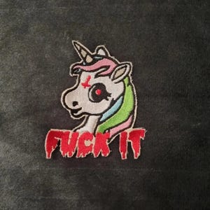 May include: An embroidered patch featuring a white unicorn head with a red inverted cross on its forehead, a black eye, and a multicolored mane in pink, blue, and green. Below the unicorn, the text FUCK IT is stitched in a dripping red font.