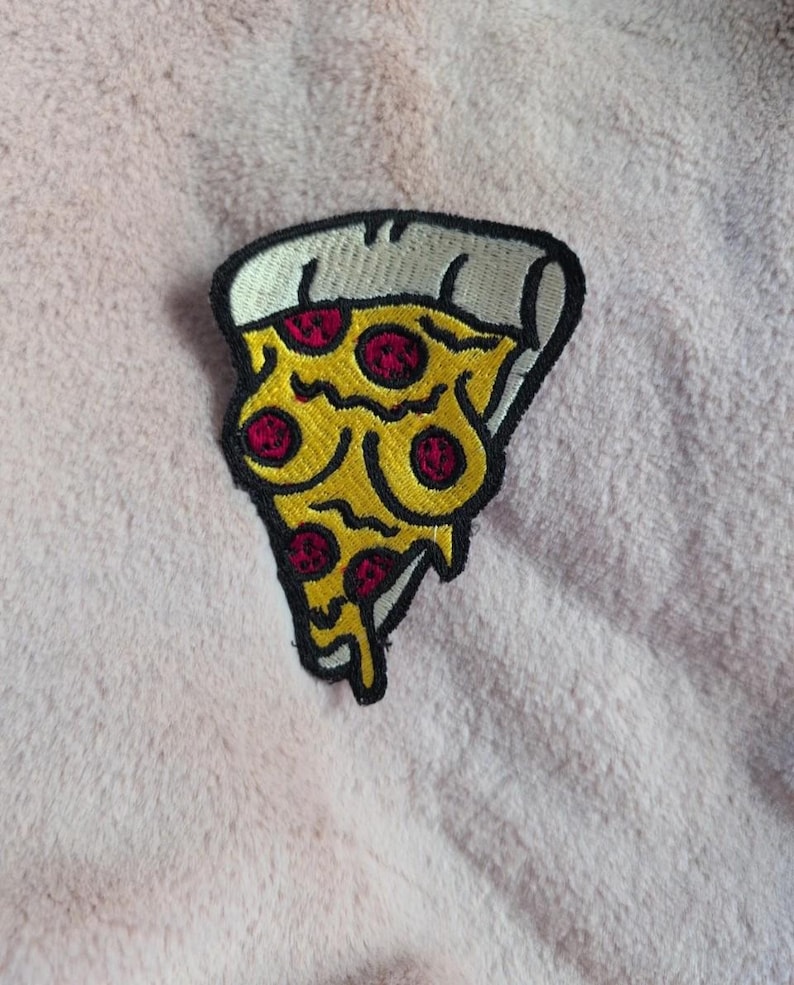 May include: An embroidered patch shaped like a slice of pizza with a thick black border. The pizza features a white crust, yellow melted cheese, and five circular red pepperoni toppings. The design has a stylized, cartoon-like appearance.