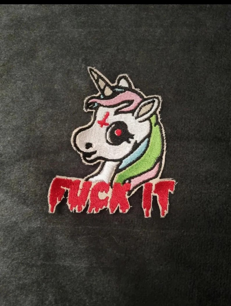May include: An embroidered patch featuring a white unicorn with a red inverted cross on its forehead, a single horn, and a multicolored mane. Below the unicorn, the text FUCK IT is stitched in red with a dripping, liquid-like effect.