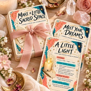 May include: A deck of cards titled Make a Little Sacred Space tied with a dusty pink ribbon, alongside two individual cards titled Meet Your Dreams and A Little Light, featuring colorful abstract shapes, gold celestial accents, and instructional text.