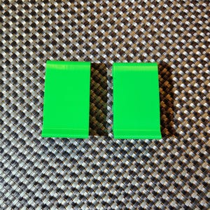 May include: Two bright green plastic stands, each featuring a smooth, angled surface and a small lip at the bottom edge to hold items in place. These objects have a simple, functional design with a solid, vibrant color and a matte finish.