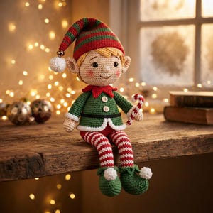 Op de afbeelding: Een gehaakte elfjespop met blond haar, met een groen en rood gestreepte muts met een witte pompon, een groen jasje met twee witte knopen en rood-wit gestreepte leggings. Het elfje houdt een kleine rood-wit gestreepte zuurstok in de hand.