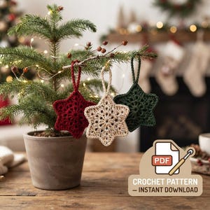 May include: Three crocheted star ornaments in dark red, cream, and dark green, each with a hanging loop. A graphic icon shows a PDF document with a crochet hook and the text "PDF CROCHET PATTERN - INSTANT DOWNLOAD" in white and brown.