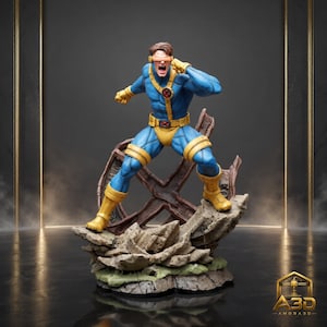May include: A detailed figurine of a superhero character in a blue and yellow costume with a red visor, standing in a dynamic pose on a rocky base with a large X-shaped structure behind, featuring the A3D AMORA3D logo in the bottom right corner.