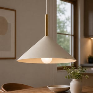 Könnte beinhalten: Eine Pendelleuchte mit einem breiten, konischen Lampenschirm in mattem Off-White. Der Schirm ist an einer zylindrischen, messingfarbenen Metallstange aufgehängt, die mit einem weißen Kabel verbunden ist. Eine runde, leuchtende Glühbirne ist sichtbar.