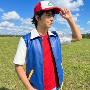以下が含まれることがあります： 緑と白のエンブレムが付いた赤と白の野球帽、白い襟と黄色のポケットのアクセントが付いた青と白の半袖ジャケット、赤いTシャツ、そして屋外の野原で着用されている水色のデニムジーンズ。