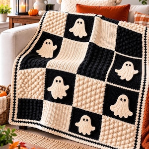 May include: A crochet blanket featuring a checkerboard pattern of black and cream squares. The cream squares alternate between textured bobble stitches and smooth ribbed designs. Each black square features a cream-colored ghost applique.