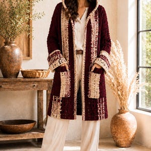 Può includere: Un cardigan lungo con cappuccio che arriva al ginocchio, di colore bordeaux intenso, con bordi in uncinetto color crema a contrasto sul cappuccio, sull'apertura frontale, sui polsini e su due tasche applicate. Il capo presenta una lavorazione a maglia.