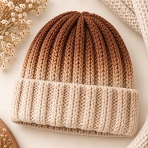 May include: A knit beanie featuring a vertical ribbed texture and an ombre color gradient that transitions from a deep brown at the crown to a light beige at the folded cuff. The hat is constructed with a thick yarn in a consistent knit pattern.