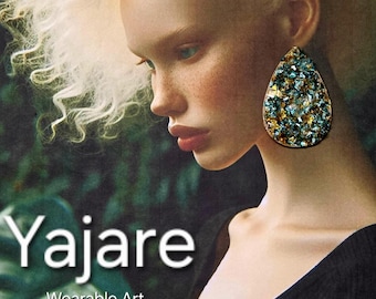 Peut inclure: Une boucle d'oreille en forme de goutte avec une surface texturée composée d'une mosaïque de fragments métalliques bleus, dorés et argentés. Le texte Yajare Wearable Art est affiché en lettres blanches sur le côté gauche de l'image.