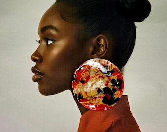 Peut inclure: Une grande boucle d'oreille circulaire imposante présentant un motif marbré abstrait et brillant dans des tons vifs de rouge, noir, blanc et or. La boucle d'oreille possède une surface lisse et réfléchissante, arborant un design audacieux.