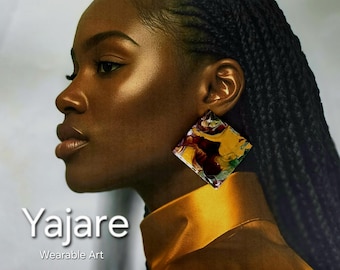 Peut inclure: Une boucle d'oreille carrée présentant un motif marbré de tourbillons bordeaux profond, jaune moutarde et blanc. La boucle d'oreille est portée au lobe et présente une finition brillante. Le texte "Yajare Wearable Art" est visible en bas à gauche.