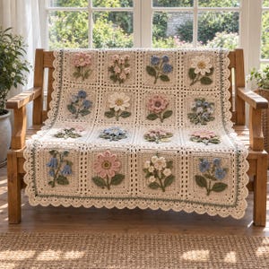 Peut inclure: Une couverture en crochet de couleur crème composée d'une grille de panneaux carrés, chacun orné d'un motif floral tridimensionnel unique dans des tons de rose, bleu et blanc, avec une bordure festonnée et une finition verte.