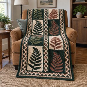 Könnte beinhalten: Eine rechteckige Häkeldecke mit einem sich wiederholenden Muster aus Farnblattmotiven in Dunkelgrün und Rostbraun. Das Design umfasst cremefarbene rechteckige Paneele, dunkelgrüne Ränder und eine komplizierte geometrische Zickzack-Bordüre.