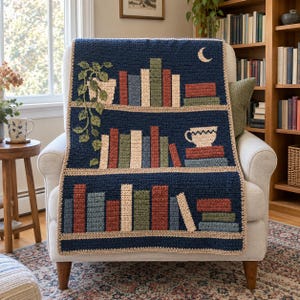 Può includere: Una coperta rettangolare all'uncinetto con sfondo blu scuro e tre ripiani orizzontali. I ripiani mostrano vari libri nei toni del rosso, blu, verde e crema, una pianta rampicante in vaso, una luna crescente e una tazza da tè su libri.