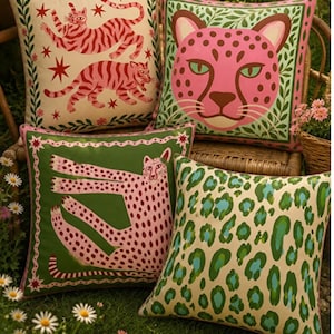 May include: Four square throw pillows featuring animal motifs. One cream pillow shows two red tigers and stars. One pink leopard face pillow has a green border. One green pillow displays a pink leopard. One cream pillow features a green and blue leopard print.
