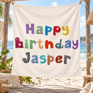 Pode incluir: Uma faixa de tecido branco com o texto Happy Birthday Jasper em letras coloridas, estampadas e texturizadas. Cada letra apresenta um design único, incluindo xadrez, bolinhas e cores sólidas, dispostas em três linhas distintas.
