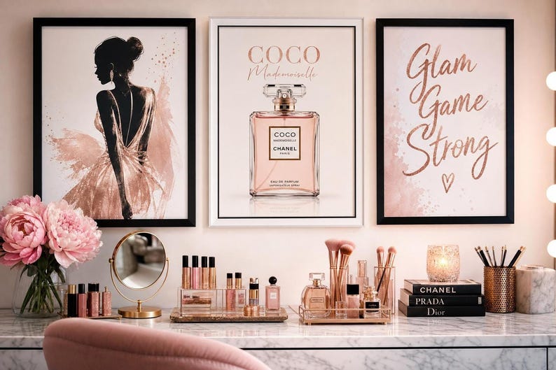 Three framed wall art prints featuring a silhouetted woman, a perfume bottle, and pink script text hanging above a makeup vanity table.