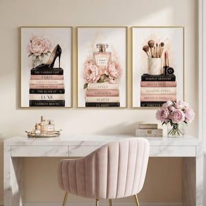 Three framed fashion art prints featuring a high heel, perfume, and makeup brushes displayed on a wall above a chic dressing room vanity.