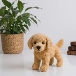 May include: A small, light tan, crocheted plush dog toy with a textured, yarn-like surface. The figure features floppy ears, a black nose, and dark, round eyes, standing in a quadrupedal position with its tail slightly raised and pointed upward.
